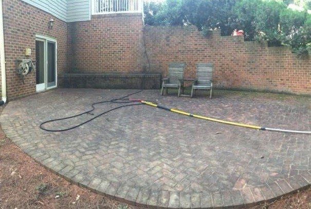 Herringbone brick patio dulled gray with grime, a hose laid across it