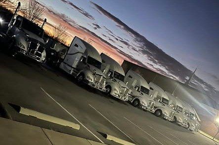 Row of clean white semi trucks parked at dusk