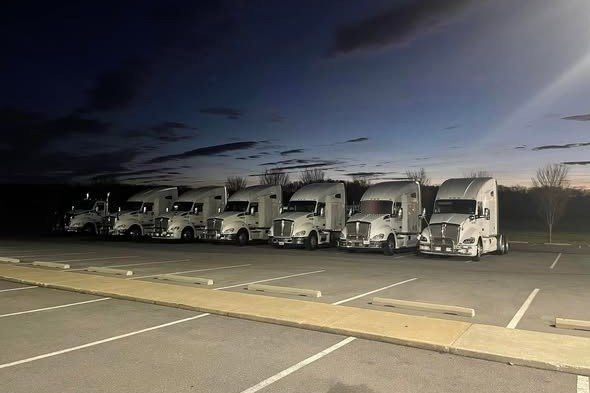 White semi trucks lined up in a parking lot at dusk after a fleet wash