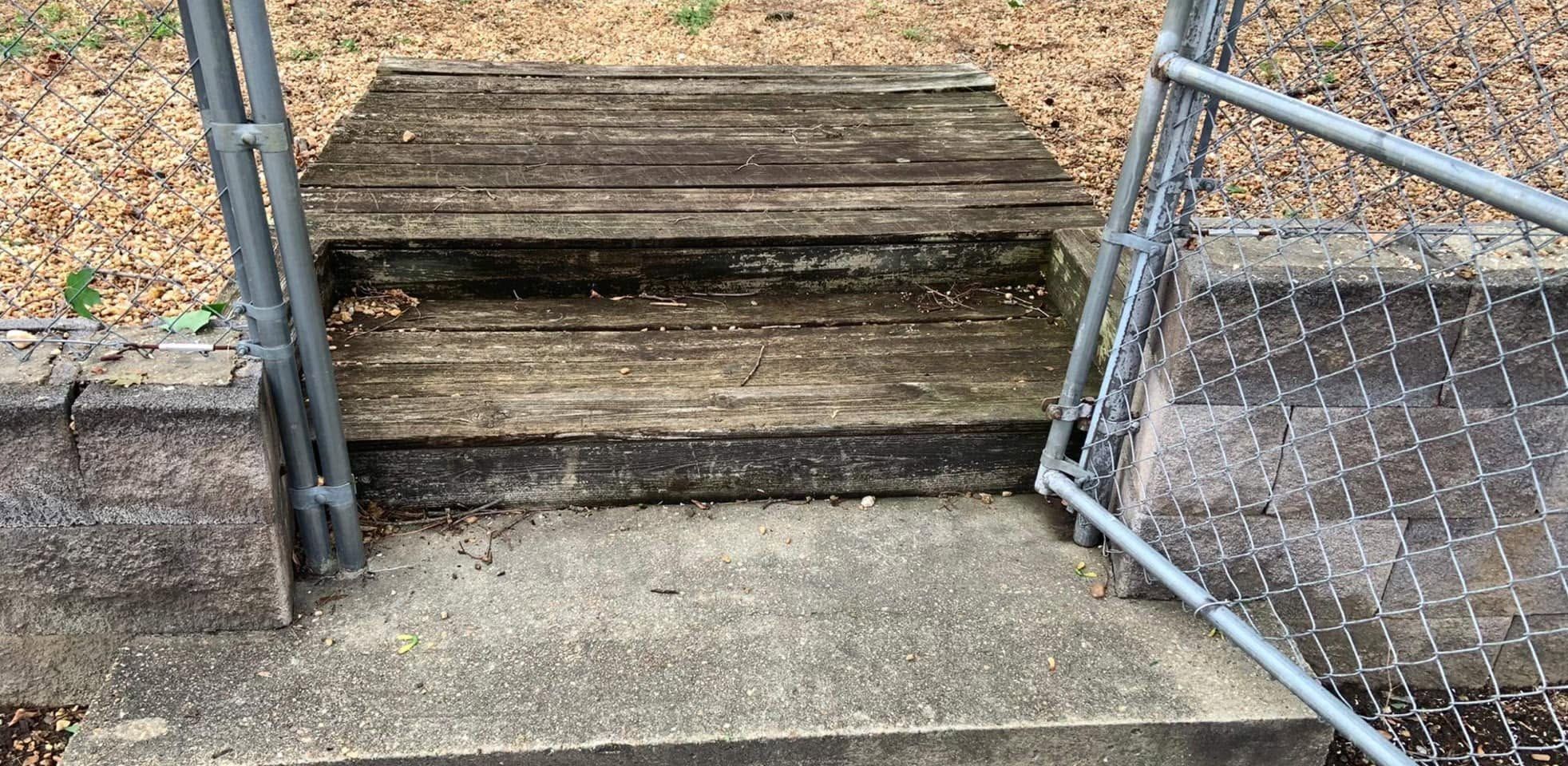 Gray, weathered wooden steps between chain-link gate posts