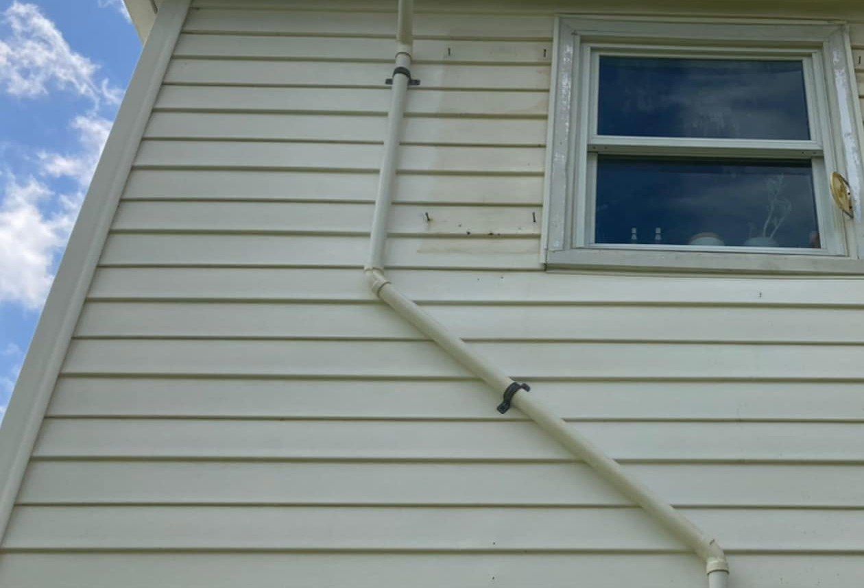 The same wall after washing, clean cream siding around the window and pipe