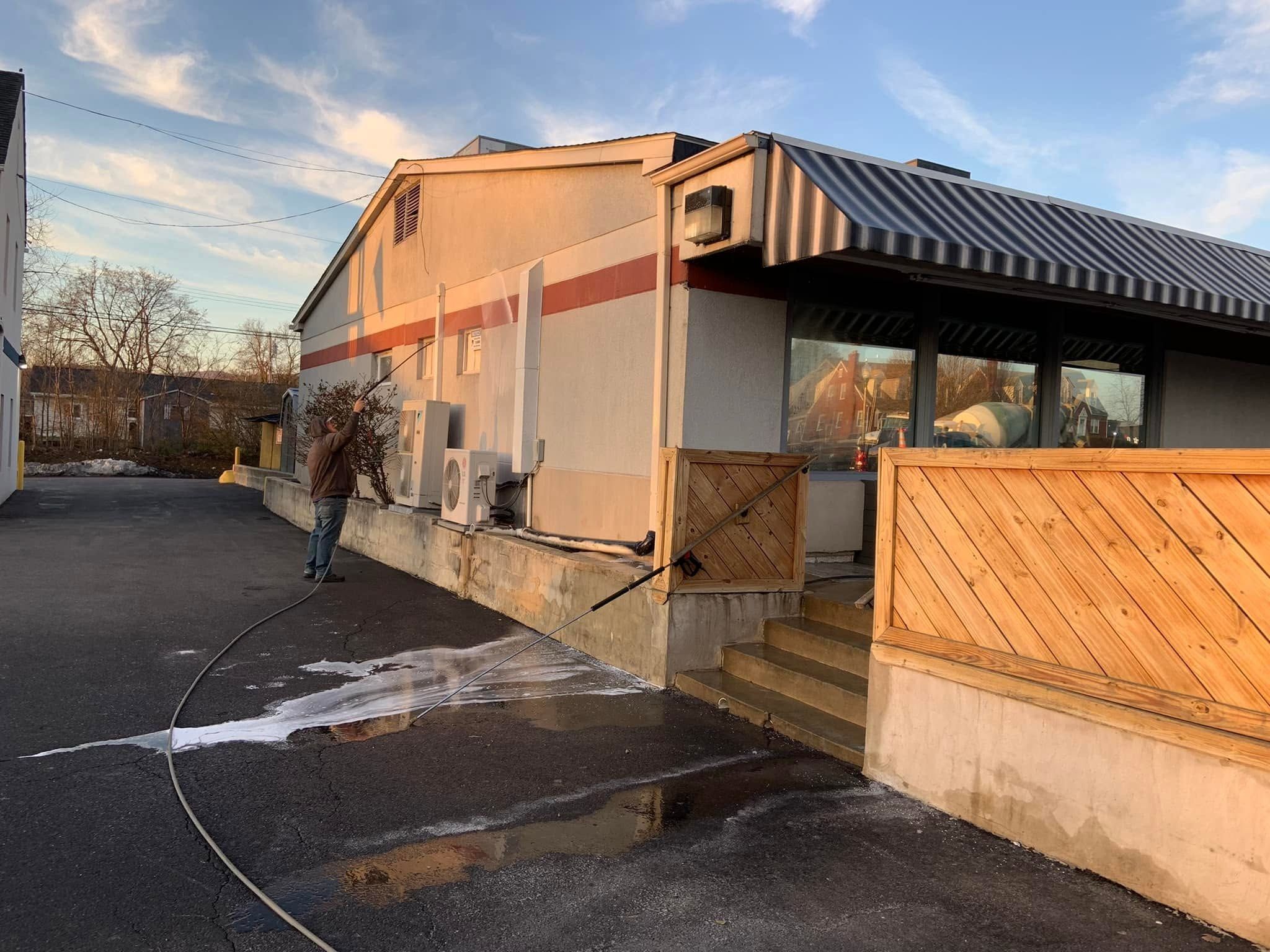 Crew member washing a stucco commercial wall with an extension wand in low, warm light, a second wand resting against the steps
