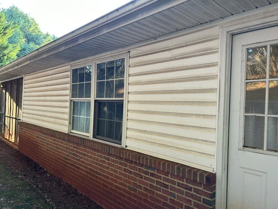Vinyl siding over a brick base with dirt streaks along every lap before washing