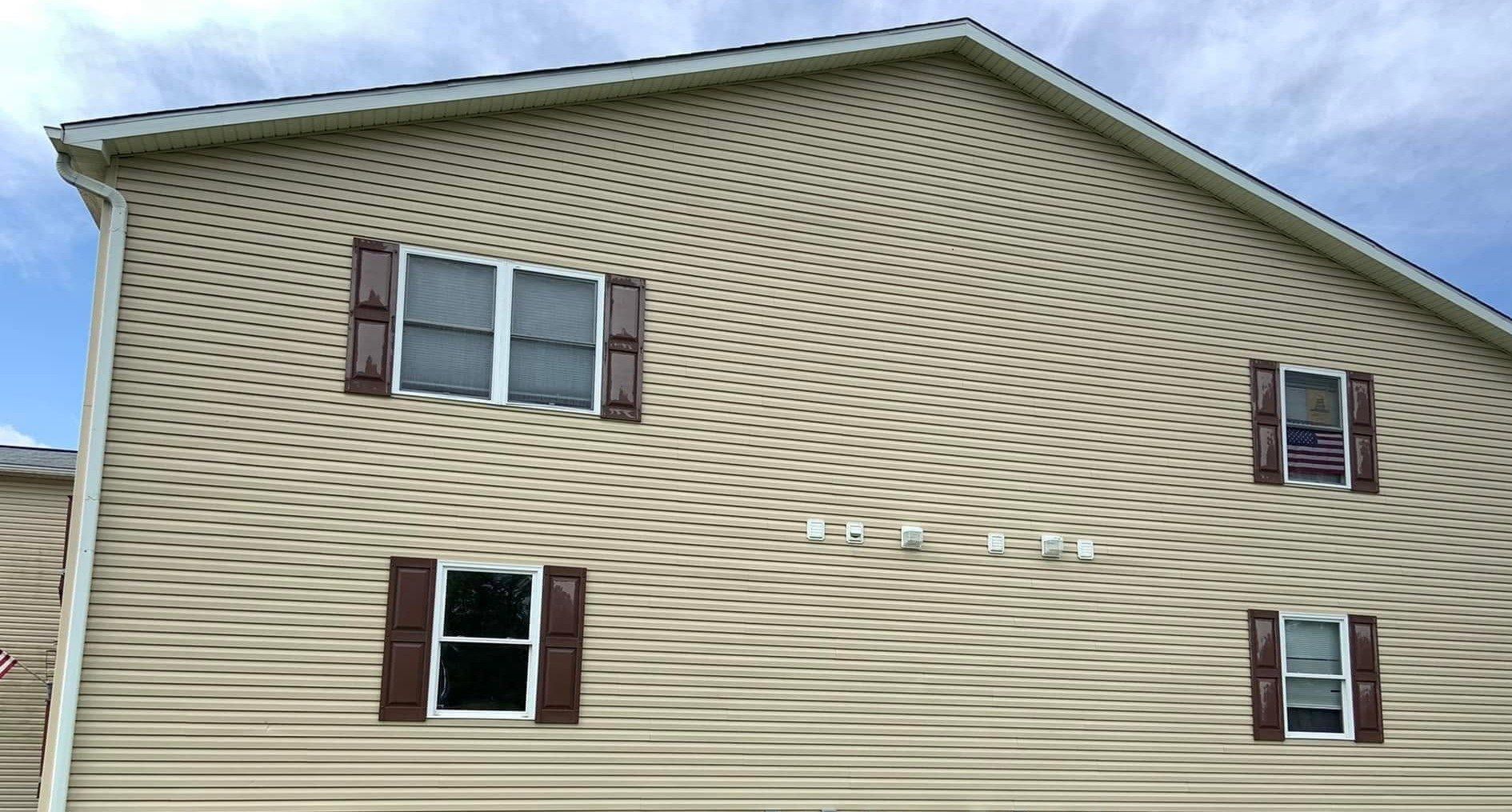 Clean tan siding on the same multi-unit gable after soft washing