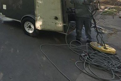 Surface cleaner and coiled hoses on the pavement behind the enclosed wash trailer