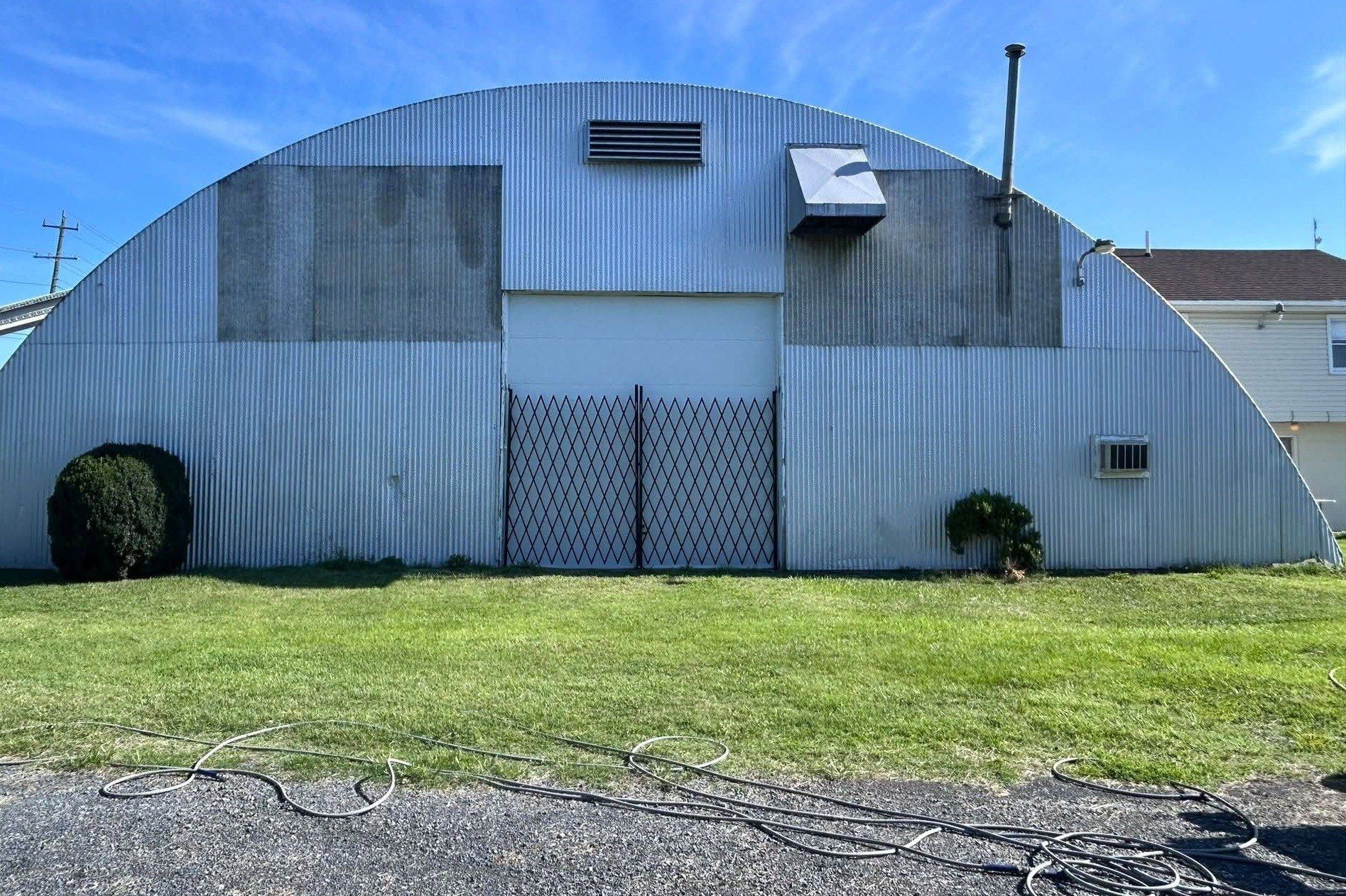 Corrugated metal building end wall mid-wash, with hoses laid out on the grass