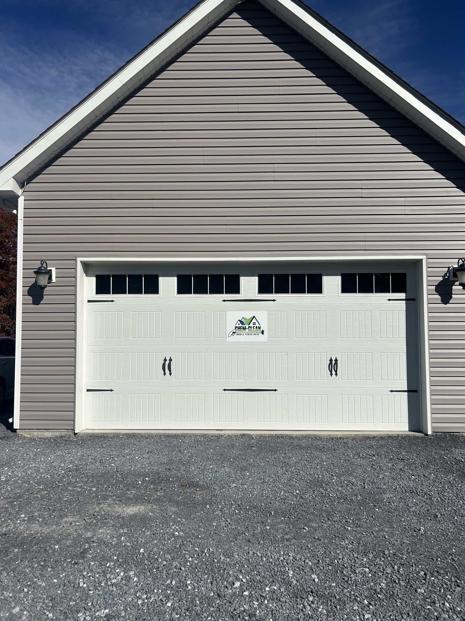 Chem-Clean Mobile Power Wash sign on a white carriage-style garage door, with taupe vinyl siding above and gravel in front