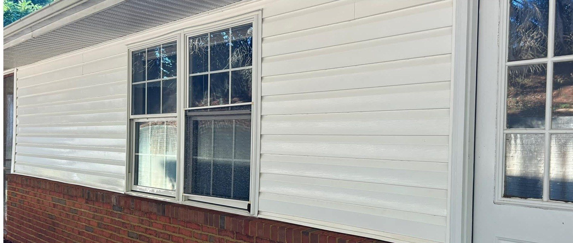 The same wall after washing, clean white siding over the brick